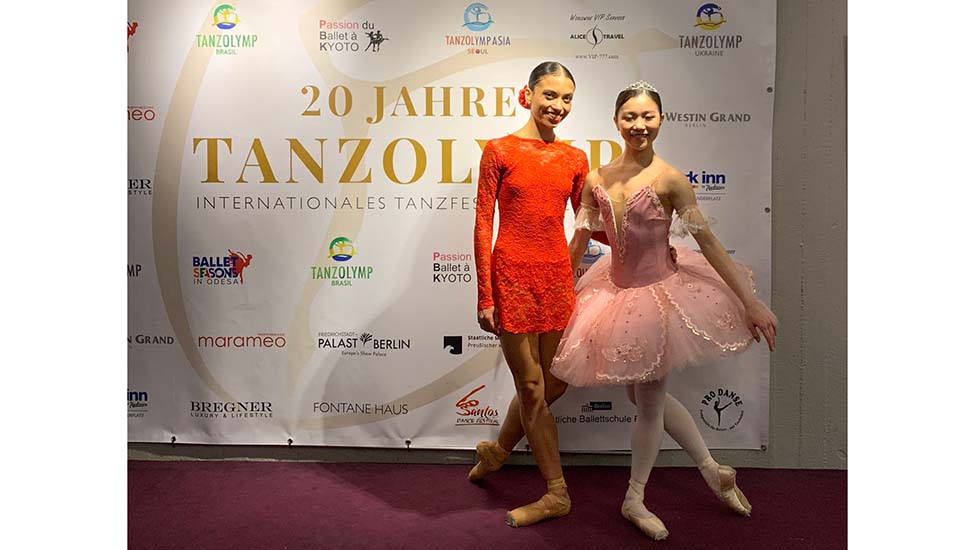 Die Tänzerinnen Rachel Pimentel Quintao Maika Kumazaki stehen vor einem Werbebanner des Tanzfestivals Tanzolymp