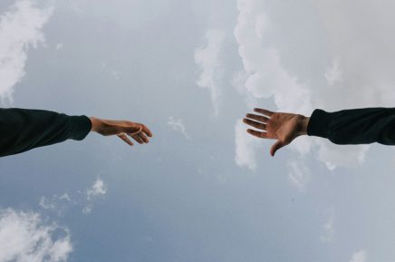 Zwei ausgestreckte Hände vor bewölktem Himmel