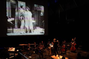 Foto vom VOLTA Ensemble auf einer Bühne vor einer Leinwand mit einem schwarz-weiß Film