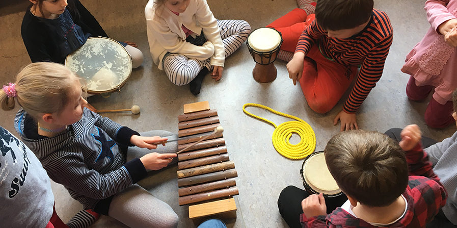 Foto von mehreren Kindern mit einem Xylophon und drei kleinen Trommeln
