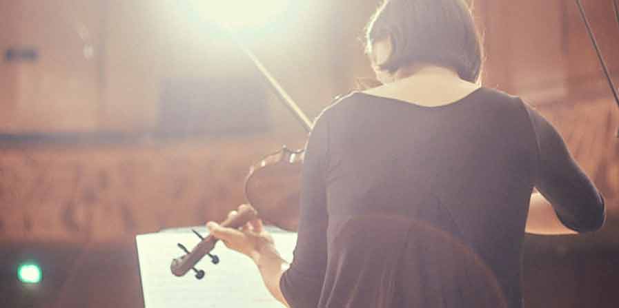 Foto von einer Frau von hinten mit Geige vor einem Notenständer