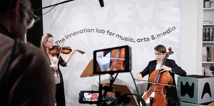 Foto von einer Geigerin und einem Cellisten, die von einer Handy-Kamera gefilmt werden